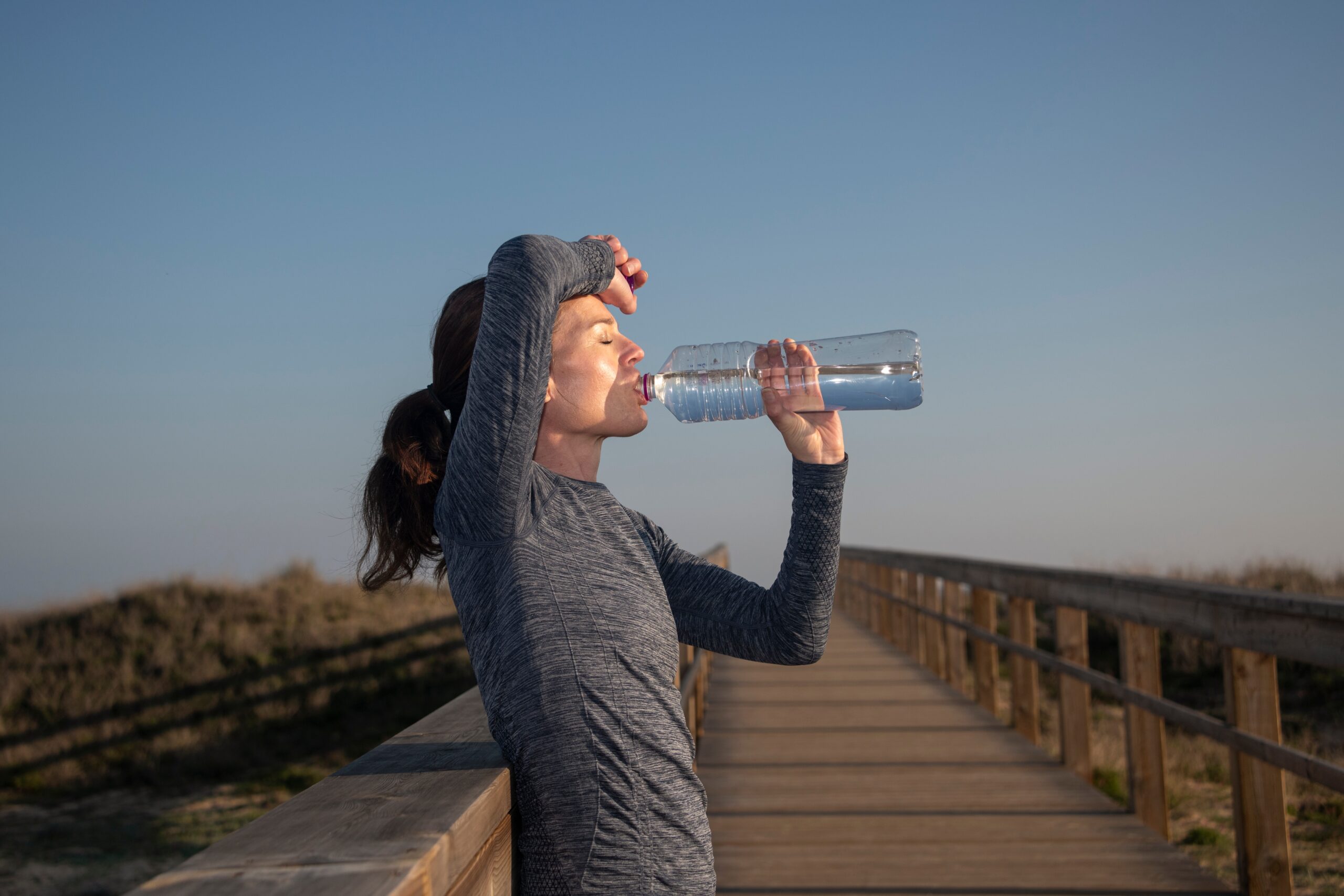 wysportowana kobieta pije w upalny dzień butelkę wody