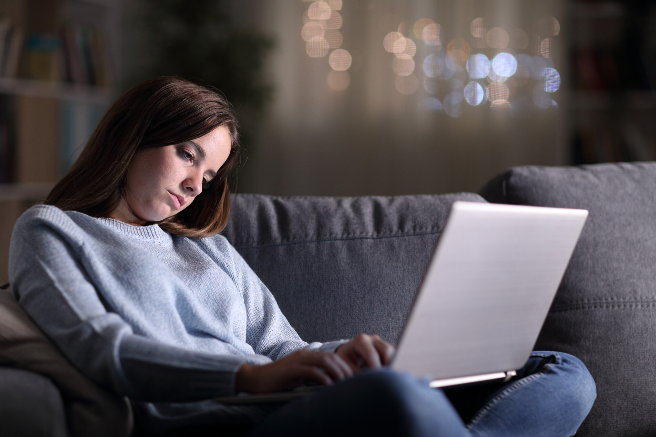 Zmęczona, śpiąca kobieta korzystająca z laptopa późno w nocy, siedząc na kanapie w domu
